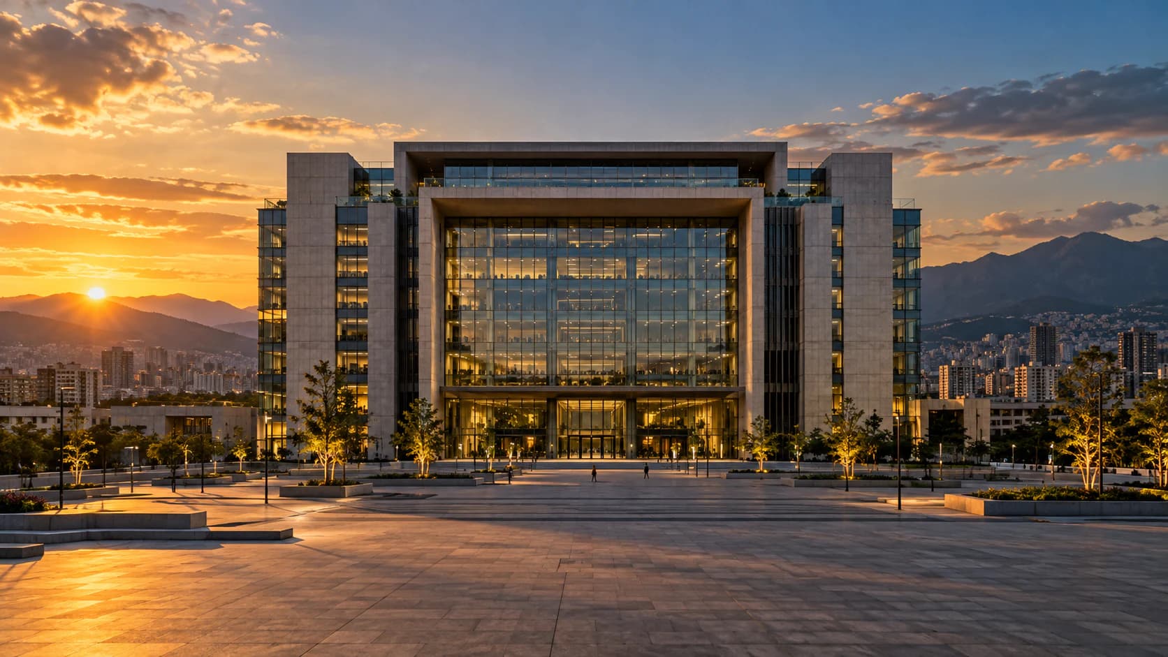 Glass-and-stone institutional headquarters with an illuminated plaza at sunset (illustrative image)